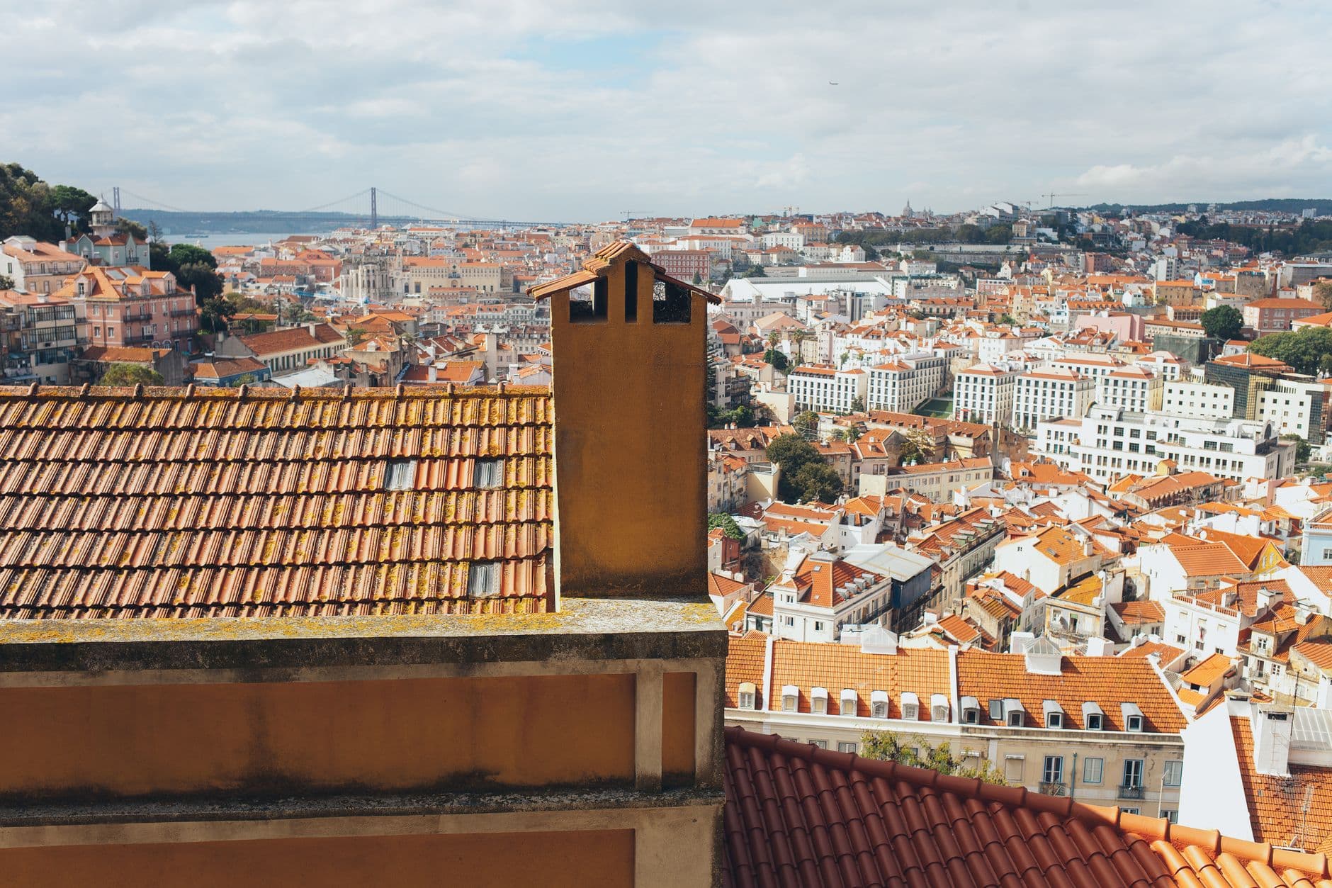 Scenic aerial view of Lisbon showcasing red-tiled roofs and historic architecture under a cloudy sky.